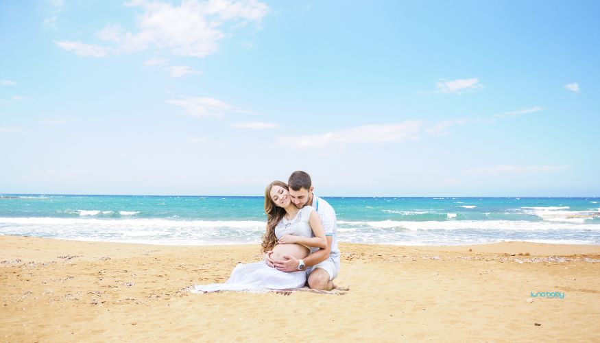 pregnant woman and her husband sitting on the beach in Miami